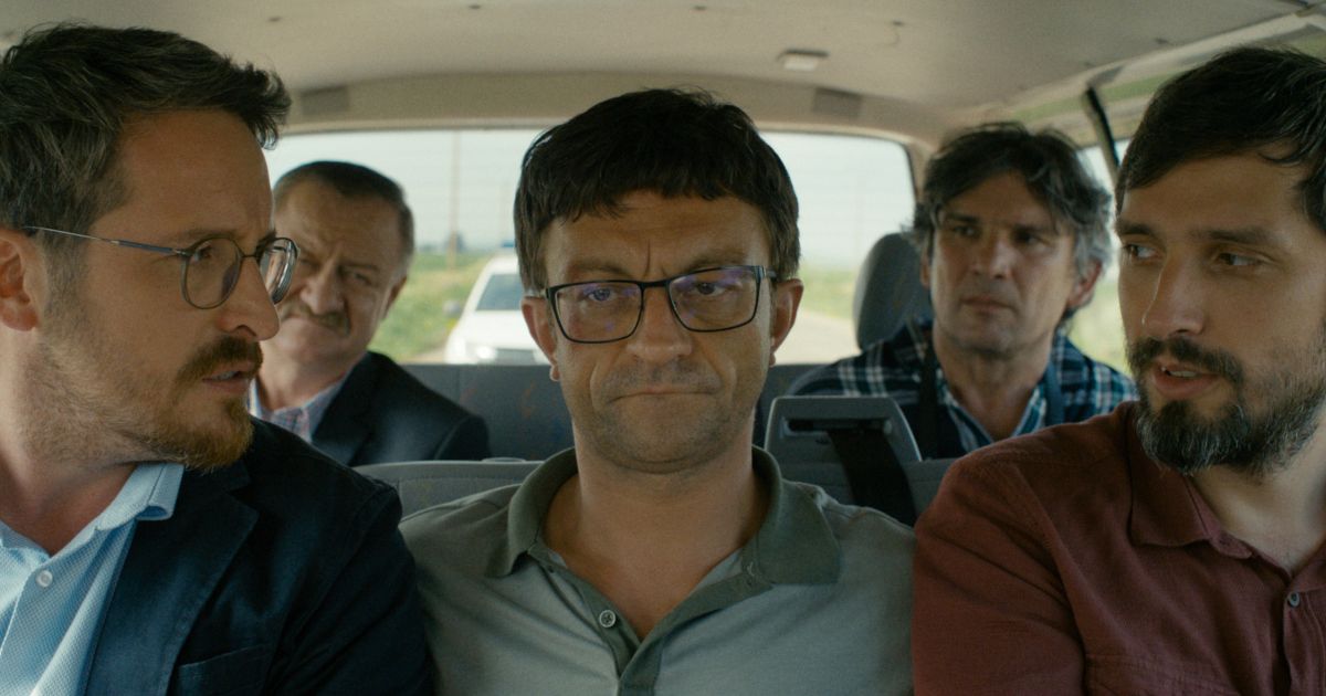 A man sits between two guys in a crowded police van in Miracle