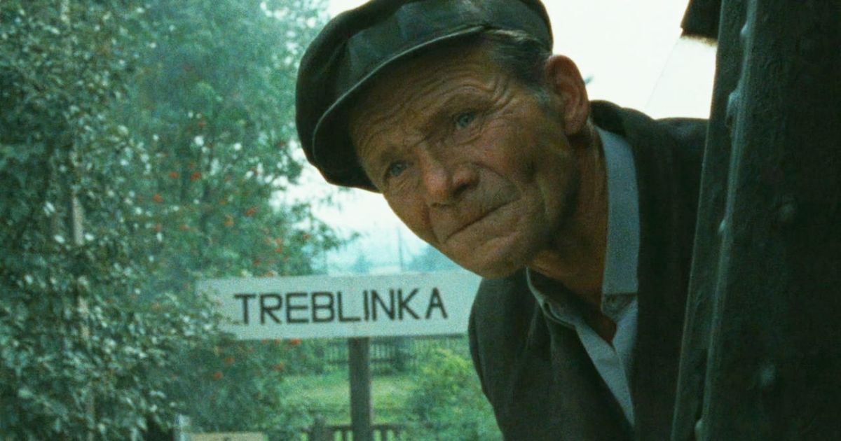 A man sticking his head out of a train while the sign Treblinka is behind him