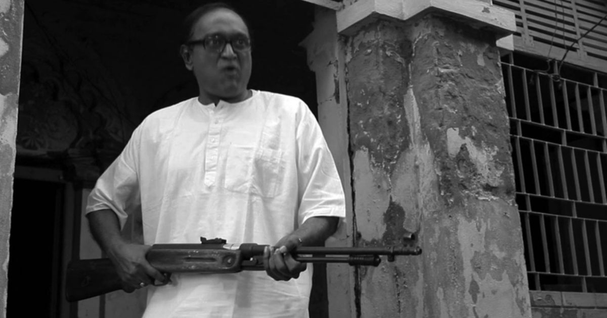 A person in Amra Ekta Cinema Banabo holding a gun as he leaves a building