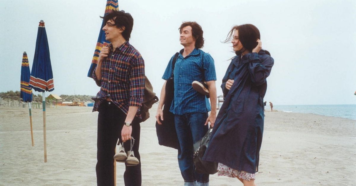A trio made of two guys and a girl standing together on a sandy beach