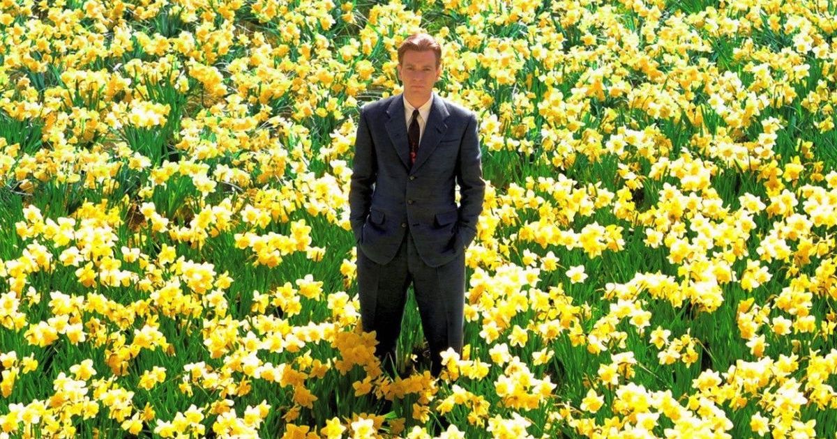 Man in suit stands in field of yellow flowers.
