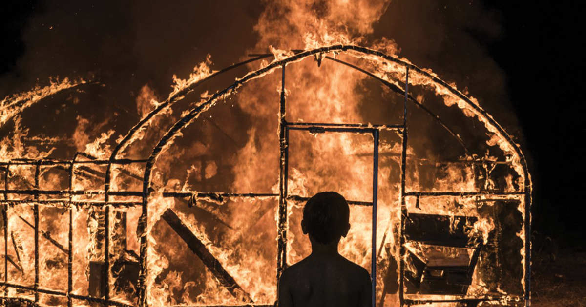 Man stands in front of burning greenhouse.