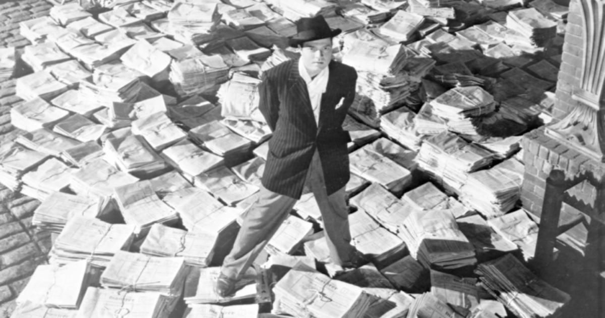 Orson Welles stands amongst a lot of newspapers in Citizen Kane 