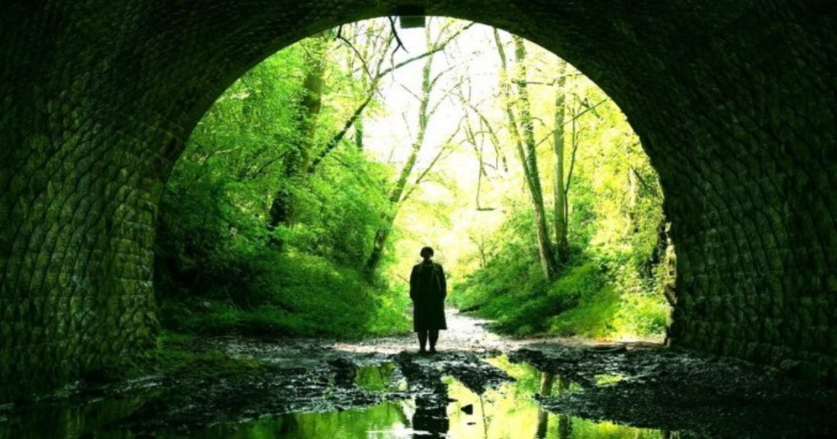 Jessie Buckley stands in a dark tunnel in the woods in Men