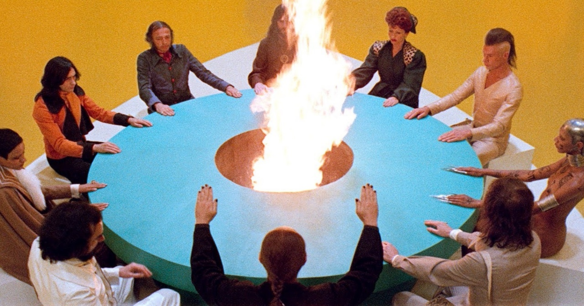 People sit around a circular table that's on fire in The Holy Mountain