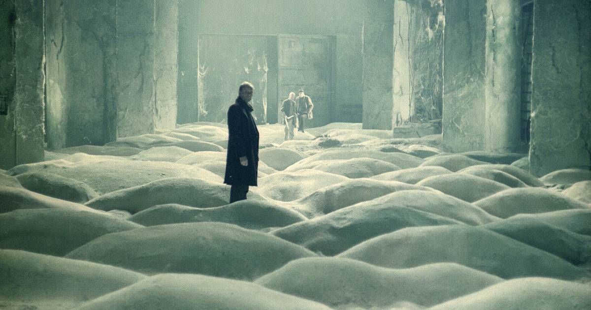 Man standing in small sand dunes inside a room in the movie Stalker