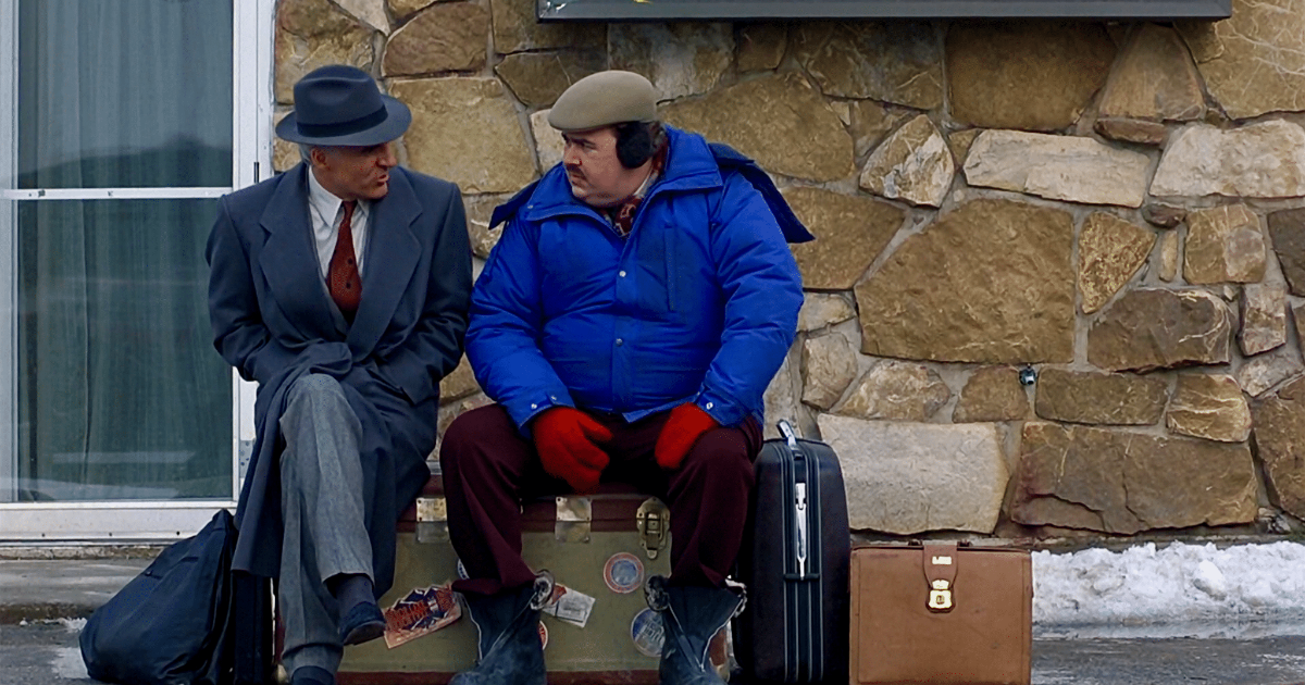Steve Martin and John Candy sitting on luggage in Planes Trains and Automobiles