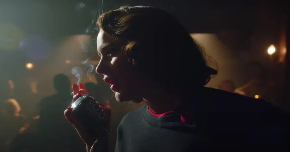 Midge smokes and speaks into a microphone in a dark club in The Marvelous Mrs. Maisel 