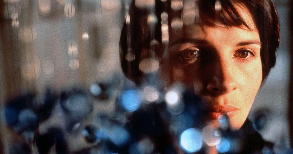 Woman stands behind blue glass chandelier hanging low.