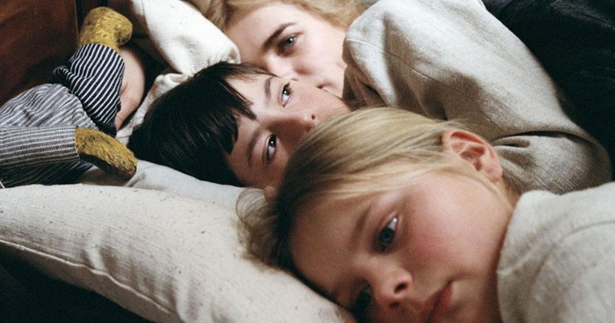 Two kids in the foreground lying on a bed while their mom lies behind them