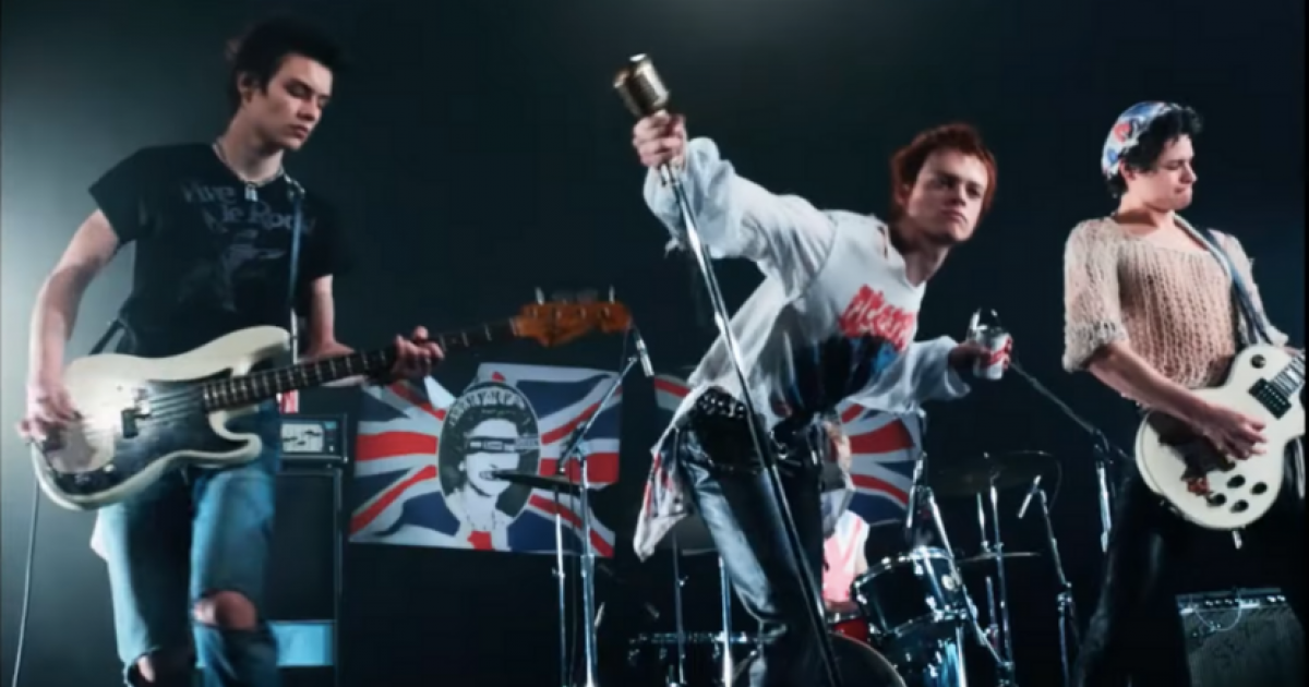 Band stands on stage in front of defaced British flag.