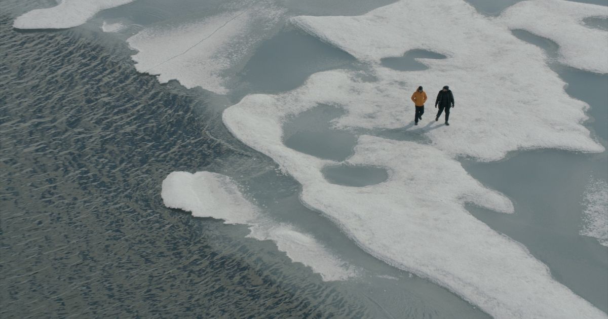 Two people walking across a thin, melting sheet of ice.