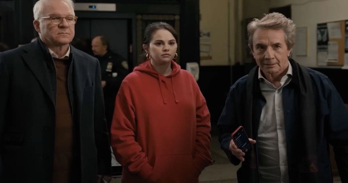 Two older men stand with a young woman in a red hoodie.