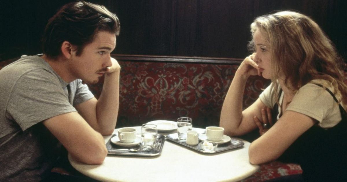 Julie Delpy and Ethan Hawke sitting and citing at a table in Before Sunrise.