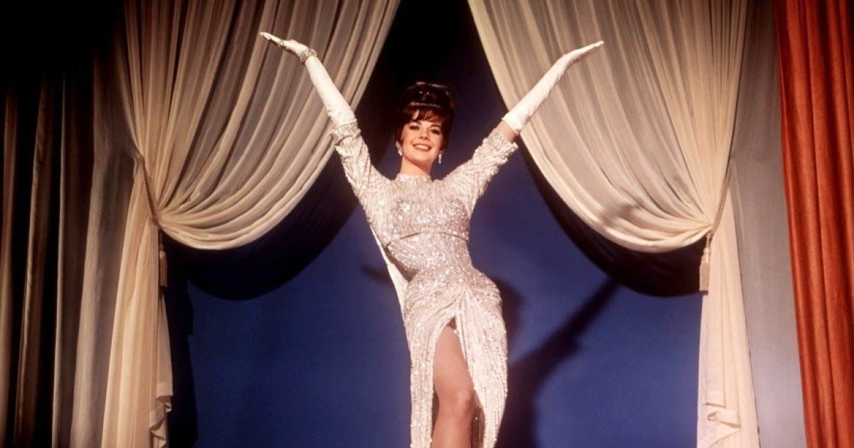 Woman in silvery white dress puts hands up, ready to perform. 