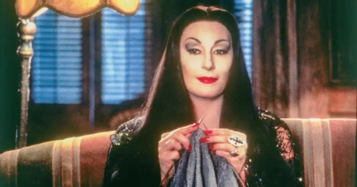 Morticia Addams (Anjelica Houston) sews as her eyes glow under the light