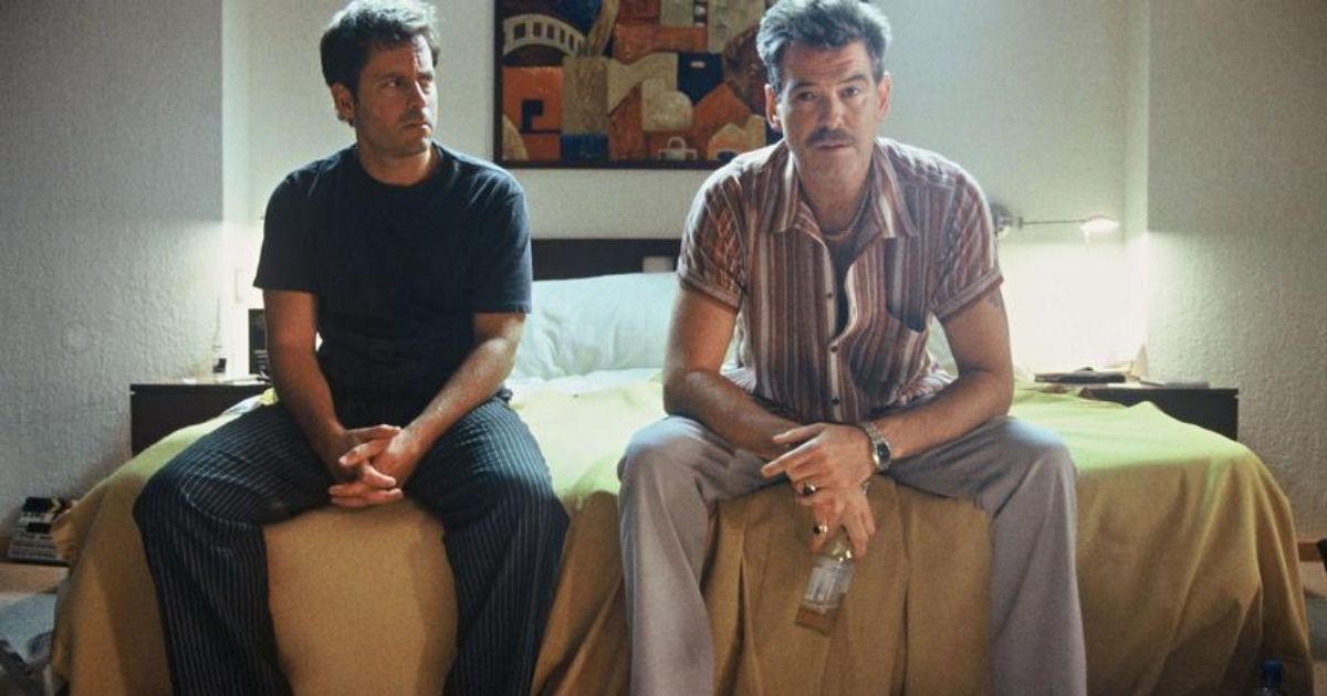 Pierce Brosnan and Greg Kinnear sitting on a bed together in The Matador