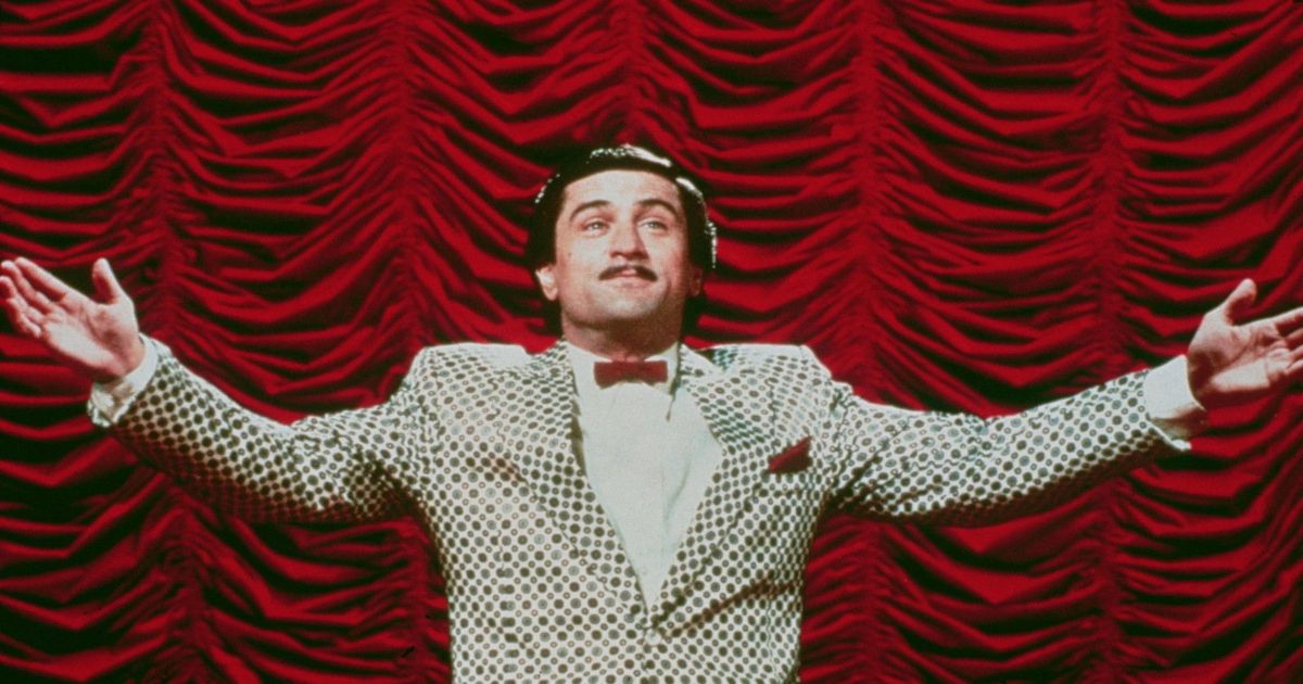 Robert De Niro spreads his arms in front of a red curtain in The King of Comedy