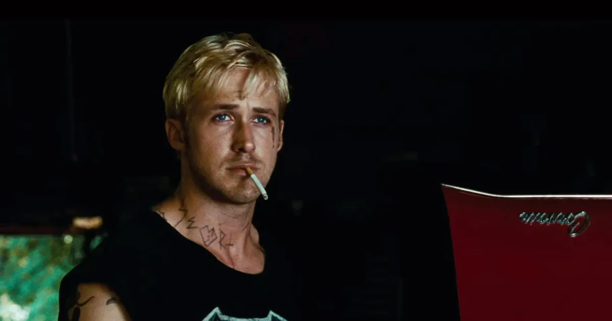 Blonde man stands with cigarettes in his mouth. 