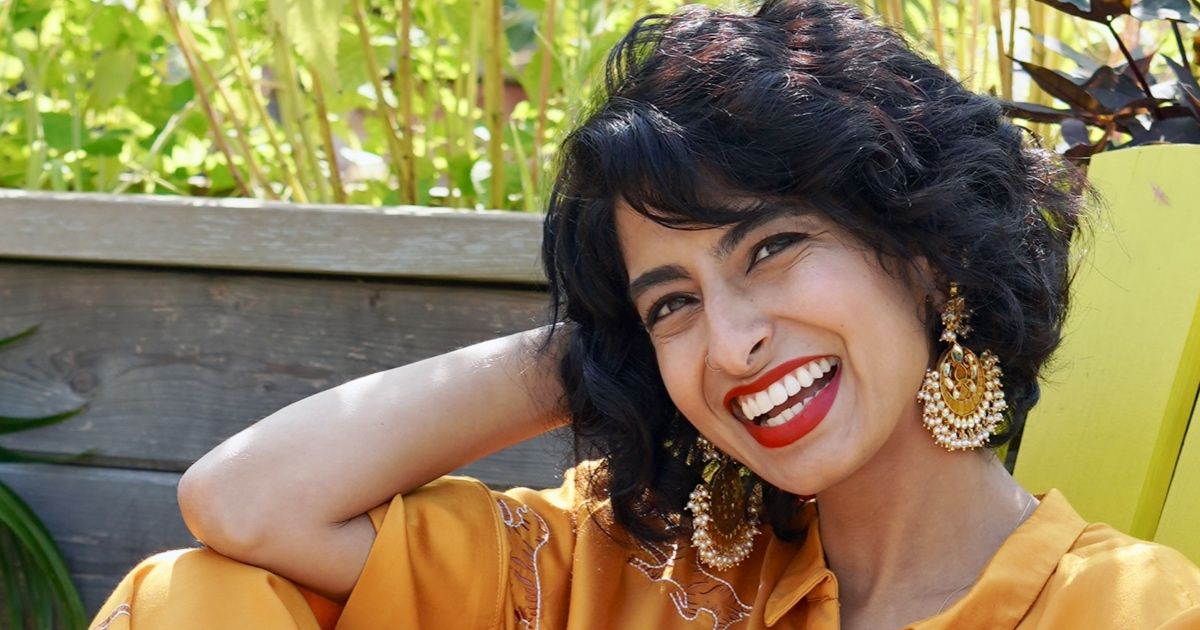 South Asian woman smiles with red lipstick while sitting in lawn chair.