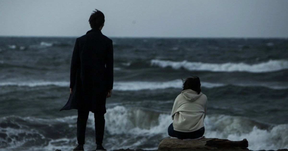 Man and woman stand/sit in front of the ocean.