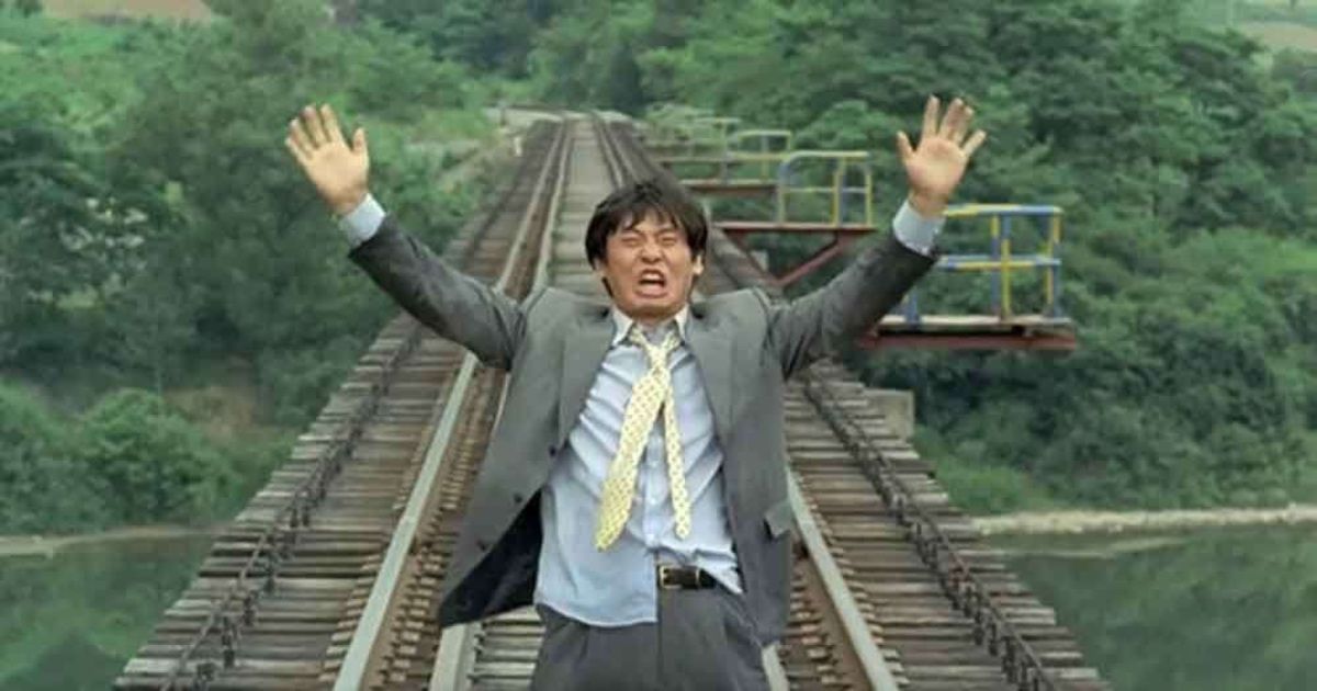 Man stands on railroad tracks with arms outstretched.