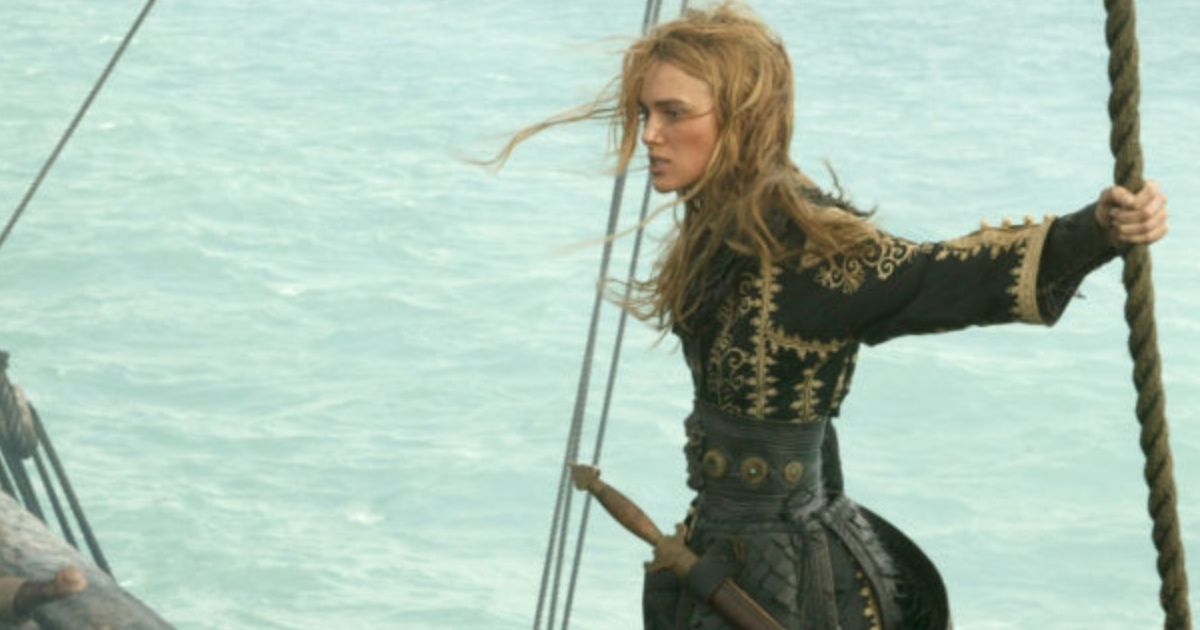 Female pirate stands on edge of ship, holding the ropes.