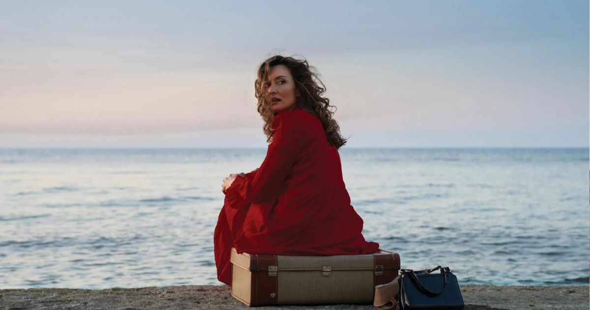 Carmen sitting at the beach with her luggage