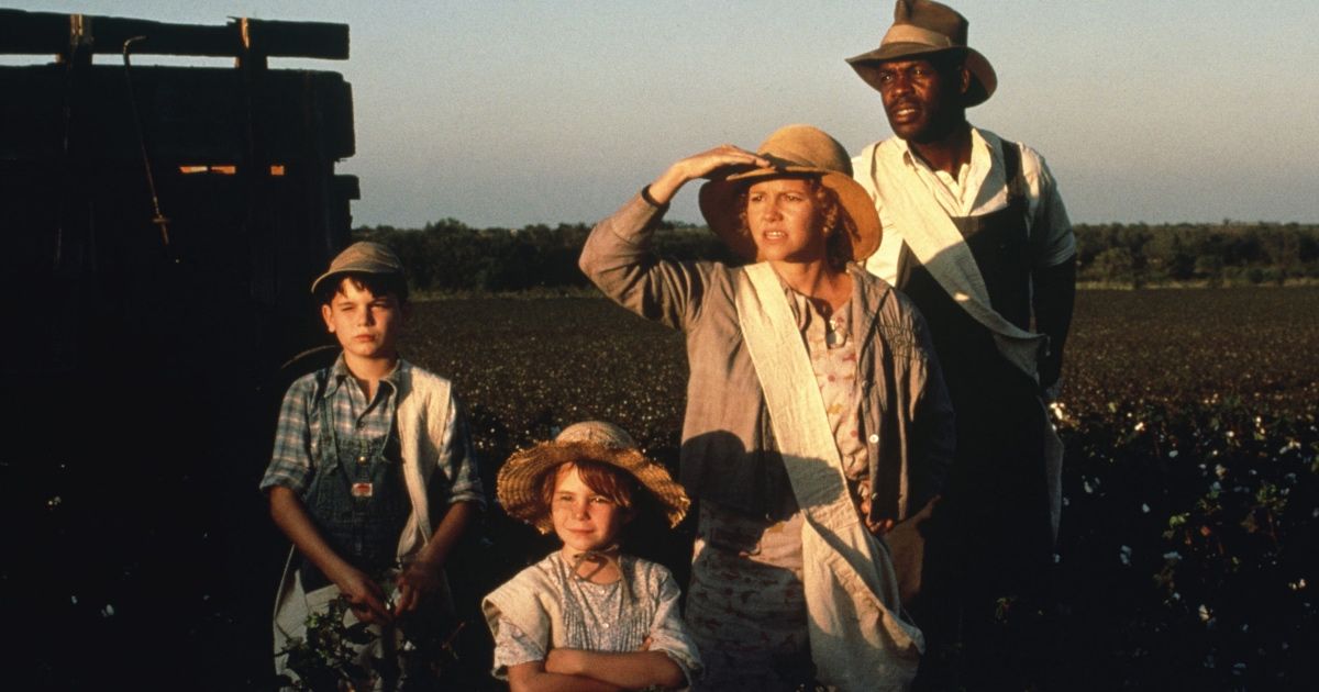 Four individuals stand in a field while sun sets.