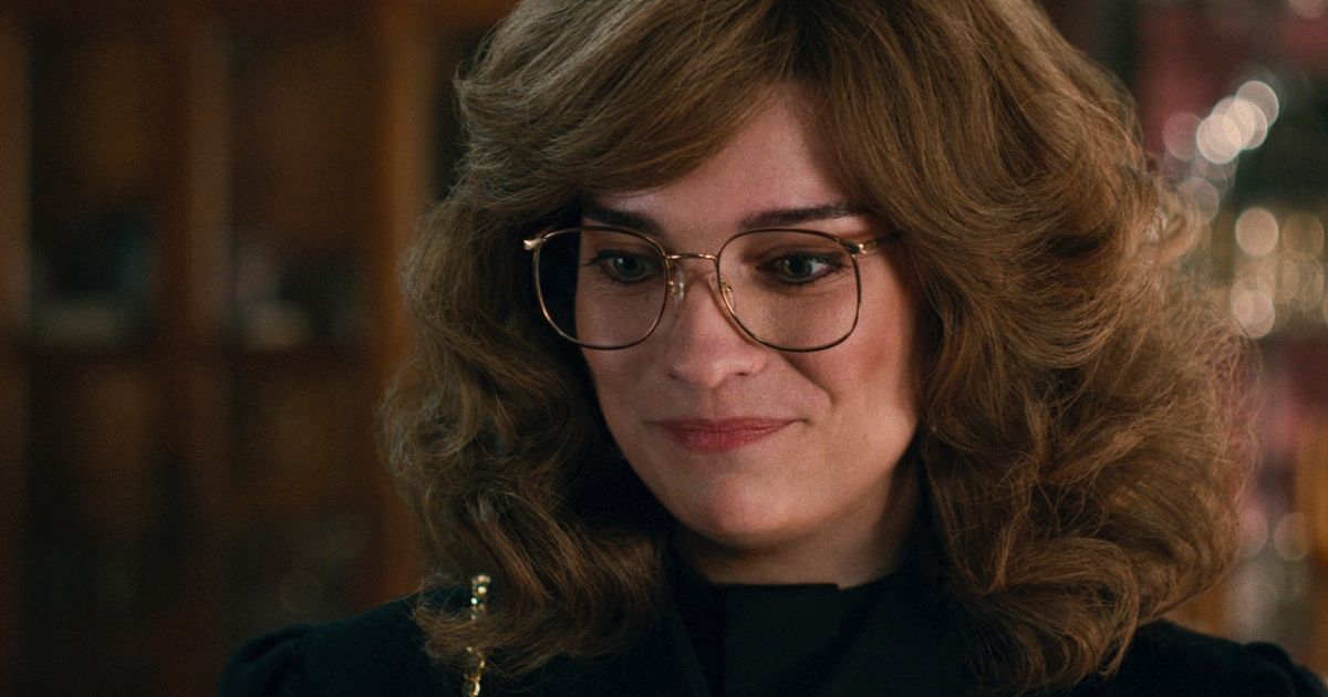 Woman with eighties hair and glasses smiles.