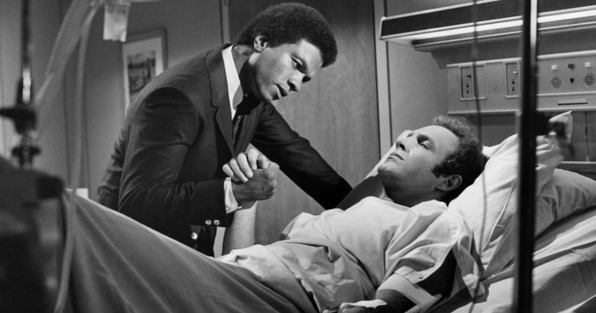 Scene from Brian's Song; Piccolo in a hospital bed and Sayers holding his hand