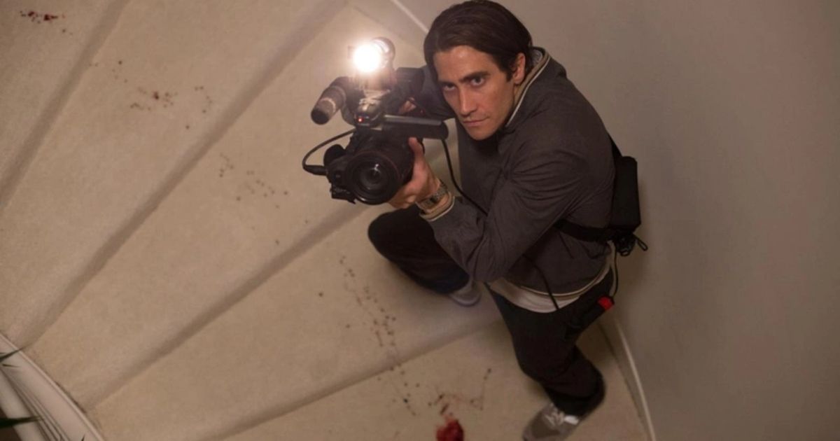 Jake Gyllenhaal preparado com uma câmera e filmando uma cena de crime em Nightcrawler
