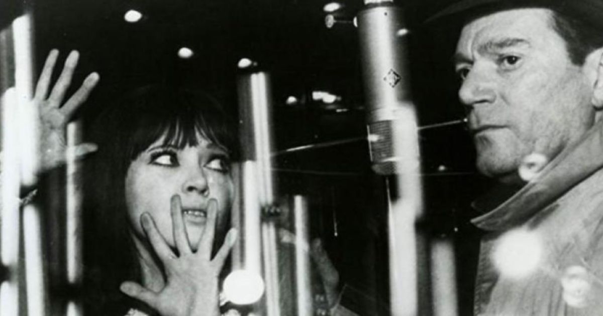 Woman looks at man while pressing palms onto glass in Alphaville movie