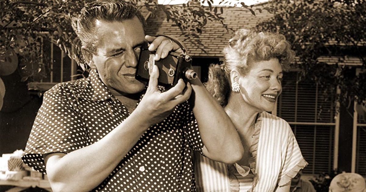 Lucille Ball and Desi Arnaz stand next to each other; he has camera in hand.
