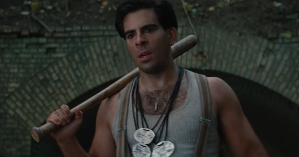 Eli Roth usando vários colares, uma regata cinza e suspensórios, carregando um bastão em Bastardos Inglórios