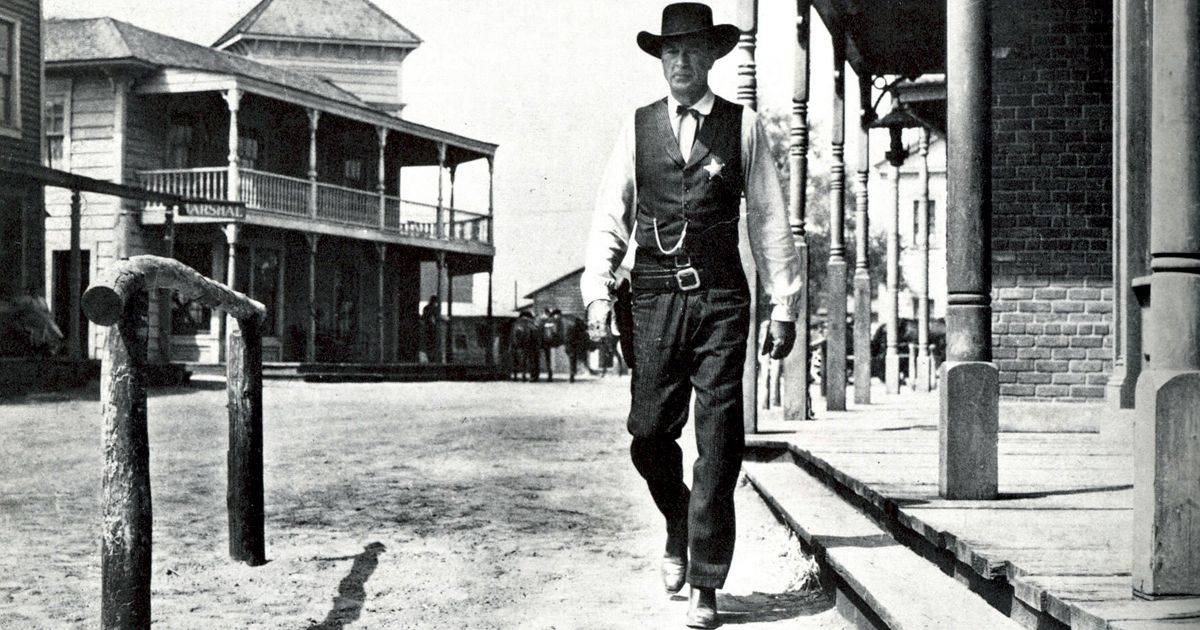 Gary Cooper em traje de xerife andando pela rua no velho oeste em High Noon