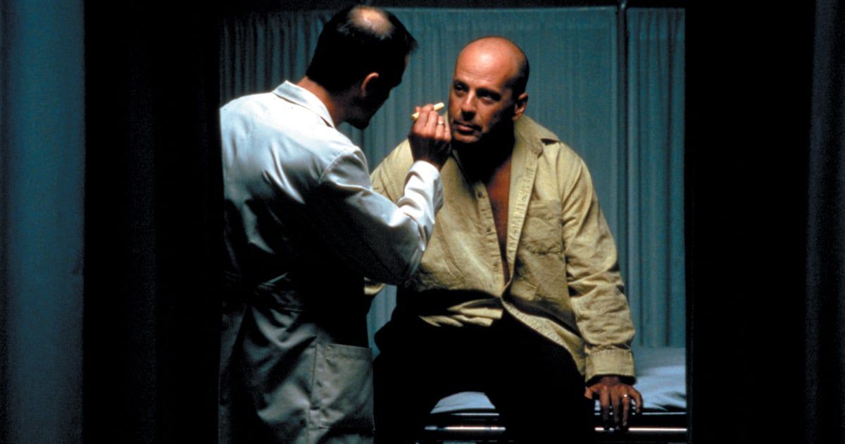 David Dunn (Bruce Willis) sits on a medial bed while a doctor shines a flashlight at him.