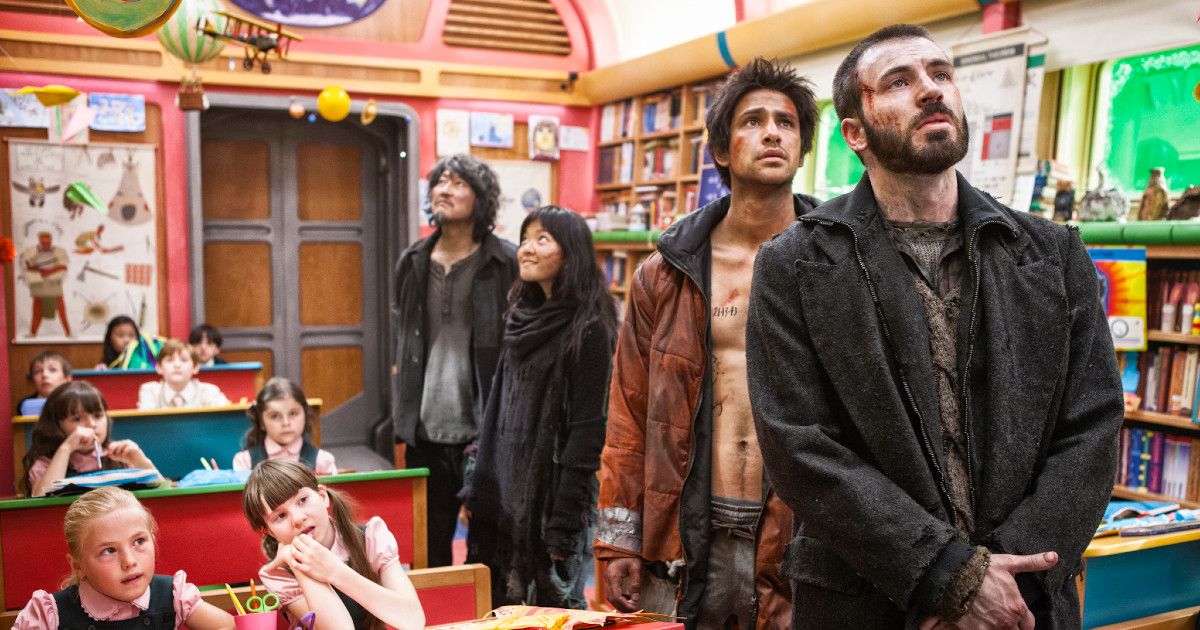 Some of the Snowpiercer (2013) cast standing in a school train car with children at desks.