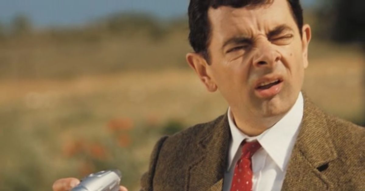Mr. Bean looks at his camera whilst on the side of the road.
