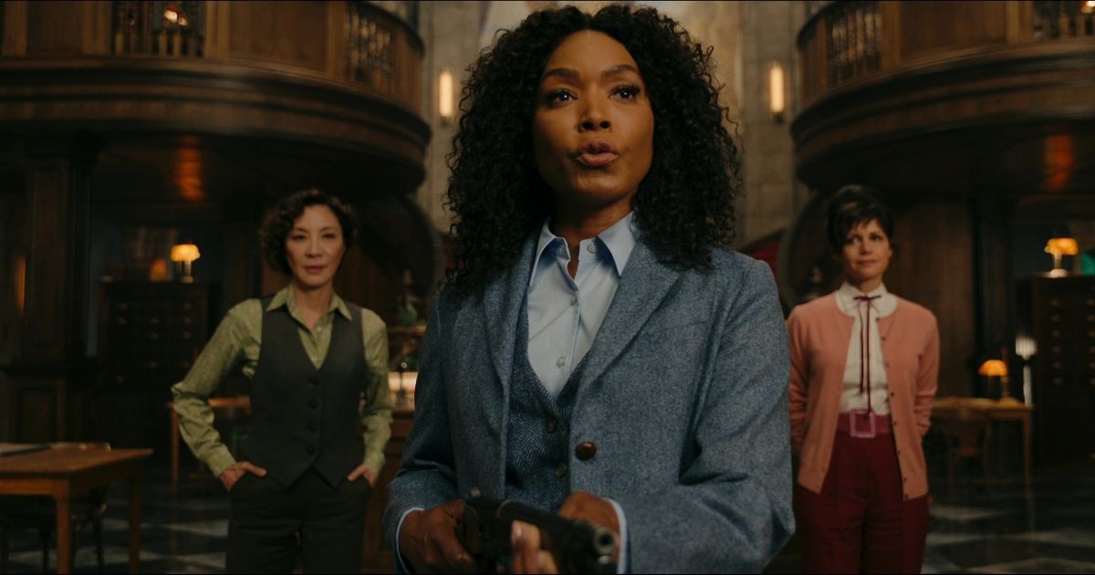A woman in a suit holds a shotgun as two other women stand behind her