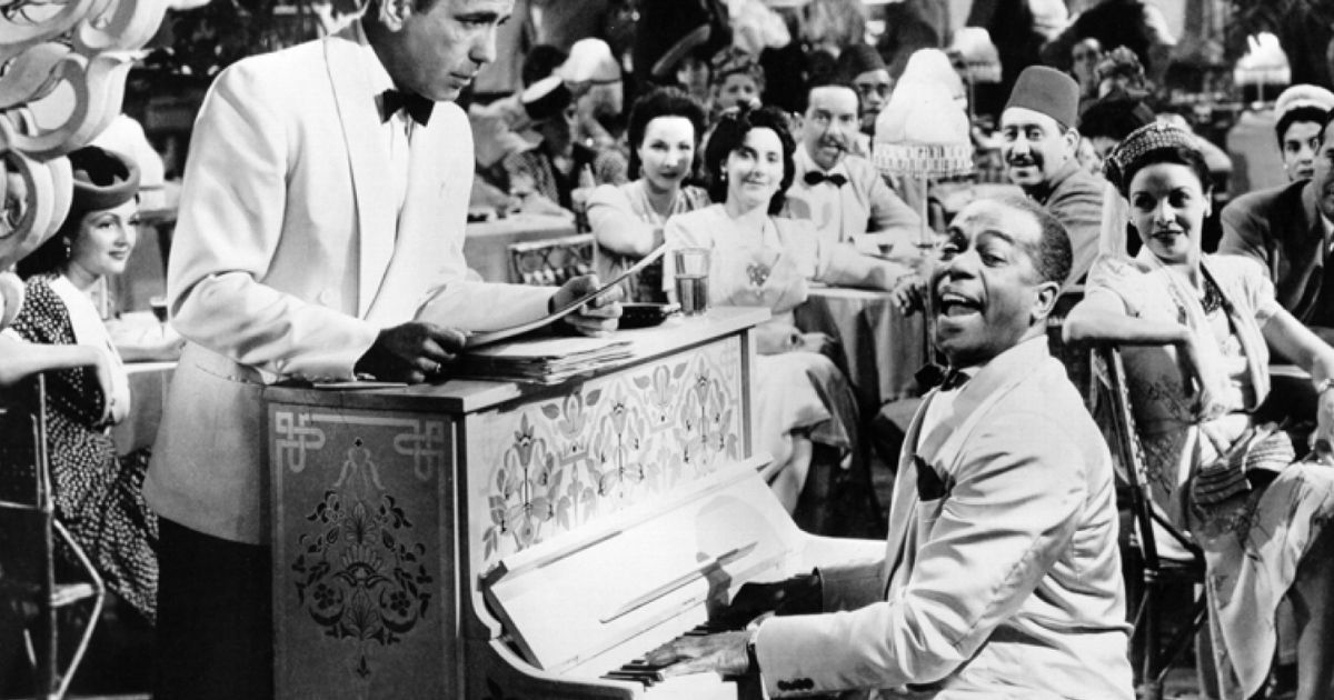 A piano player entertains a party in a bar while his boss stares at him in Casablanca film from 1942