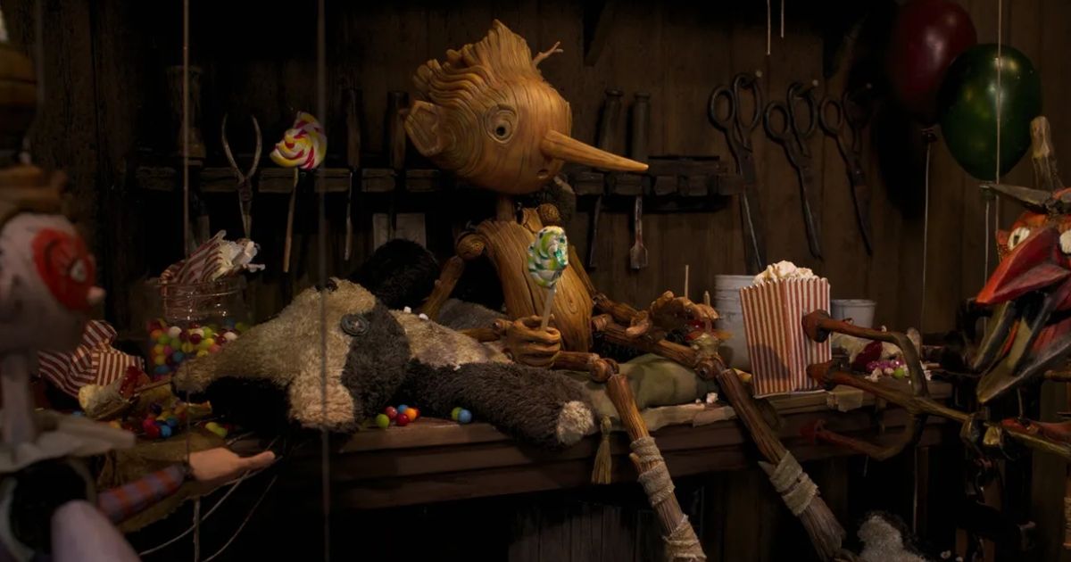 Pinocchio sits on the table in Geppetto's shop surrounded by strange tools. 