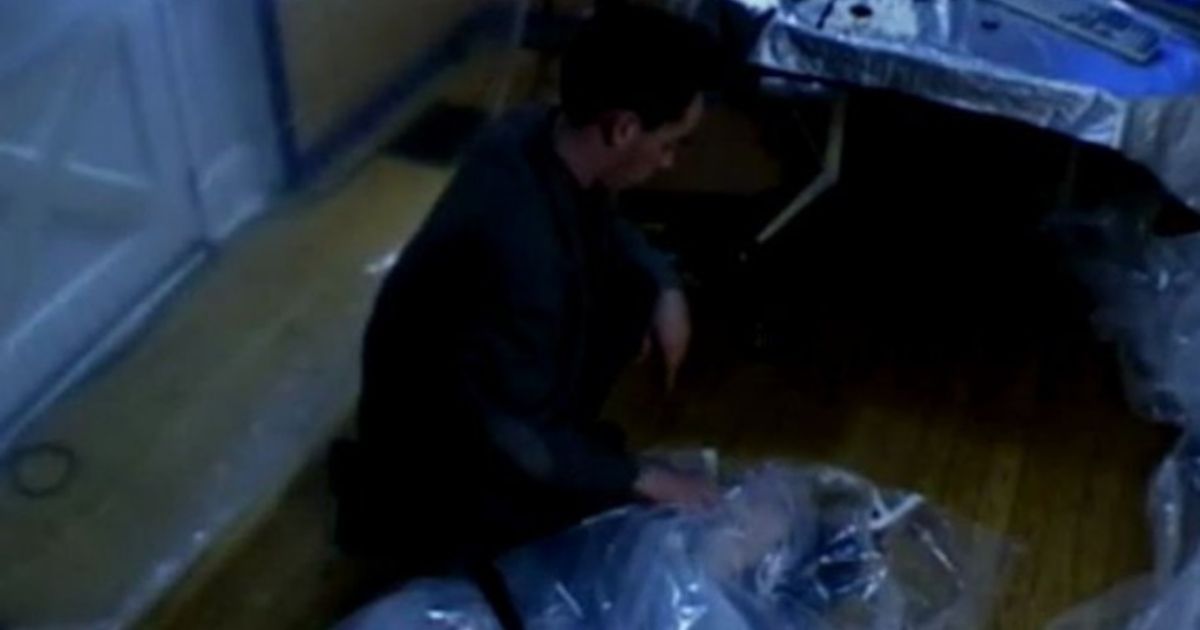 A man kneels beside a body covered in plastic in The Last Broadcast