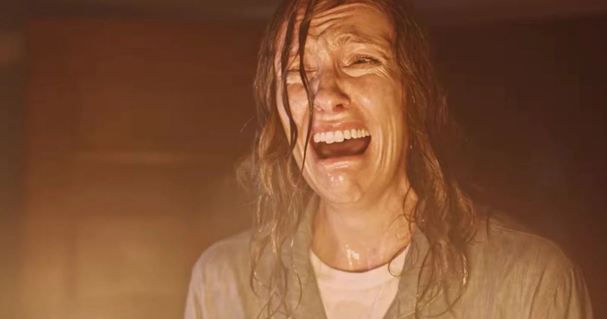 Toni Collette as Annie, soaking wet with her hair dripping as she looks at a fire in her living room while she hysterically cries in in Hereditary
