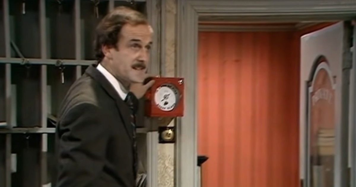 Basil stands in front of the fire alarm in Fawlty Towers