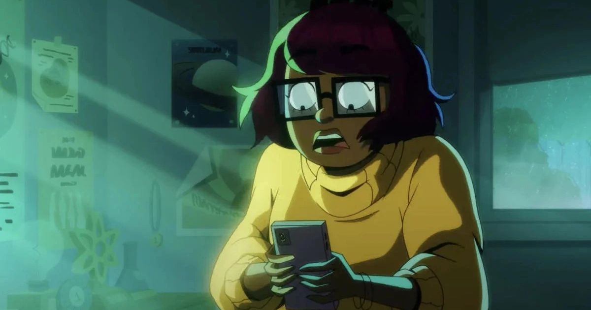 Velma looking down at phone in shock, in front of a green and white bulletin board.
