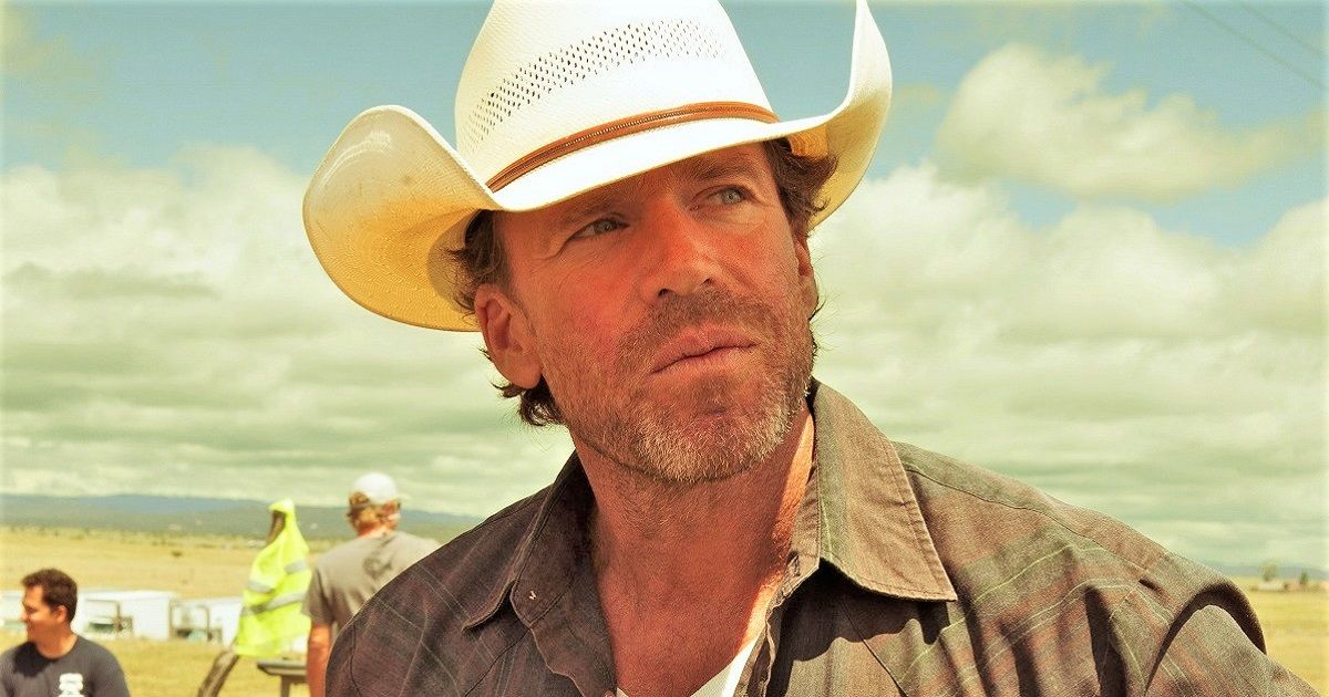 Taylor Sheridan on set wearing a flannel shirt and cowboy hat.