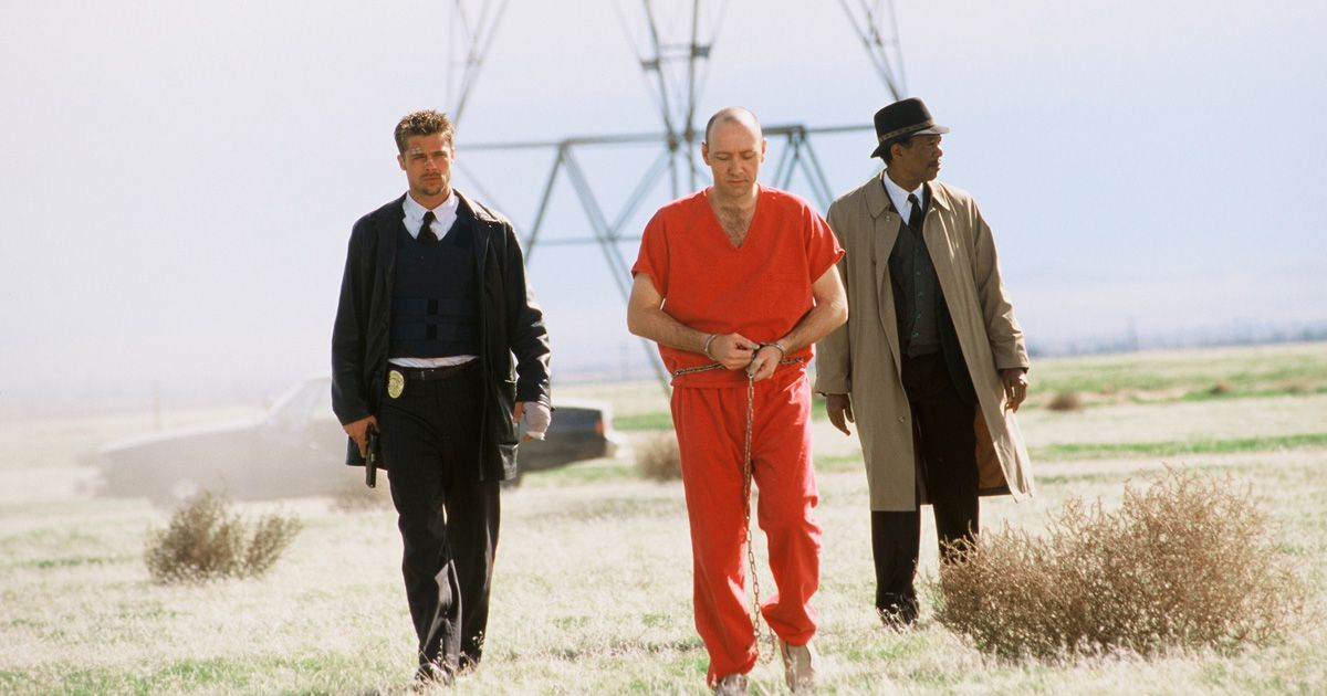 two policemen and a prisoner in an orange jumpsuit walking in the desert