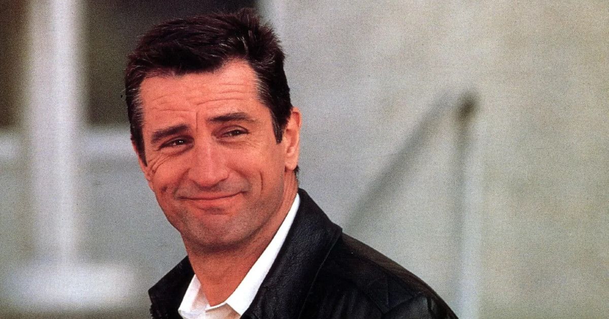 Robert De Niro wearing a black jacket and white shirt, turning around and smiling in Midnight Run.