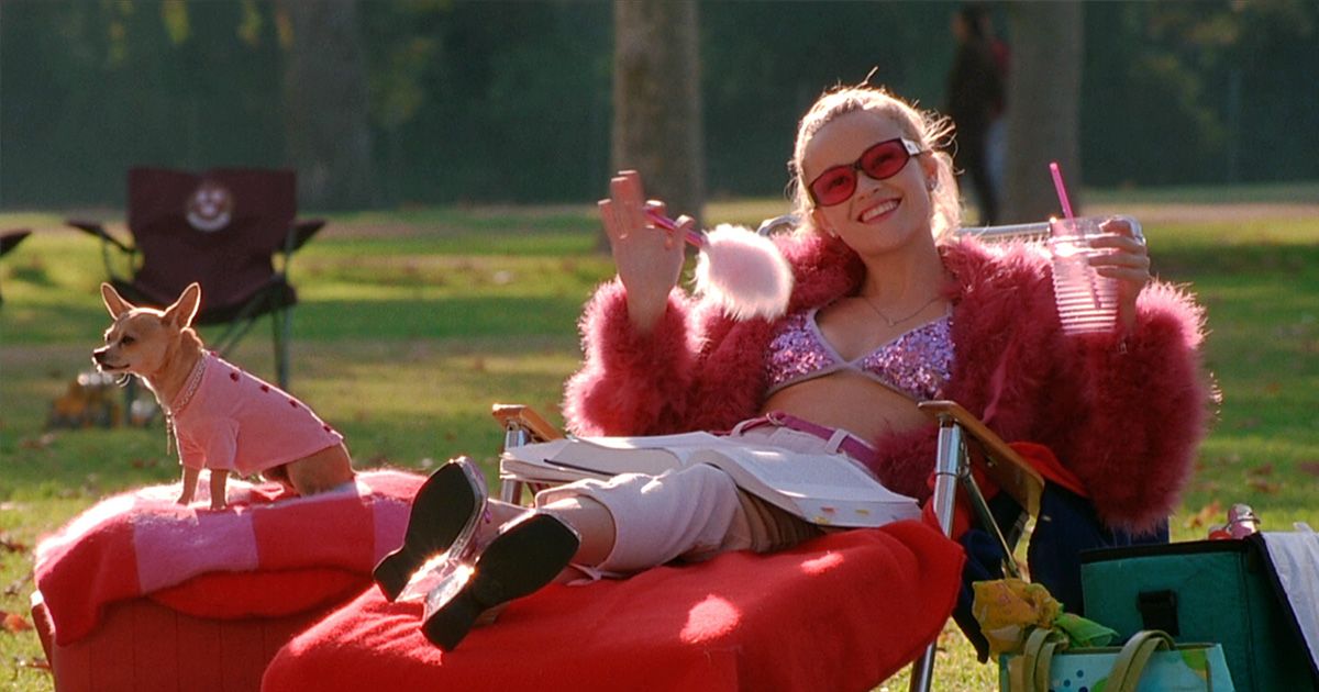 woman in sparkly pink bikini on a red longue chair outside holding a drink with her dog next to her